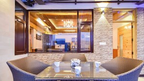 A dining area with wicker chairs and a glass table, a chandelier, and a view of the interior through a glass door. - The Castle Villa Hill View kasauli (Kasauli)