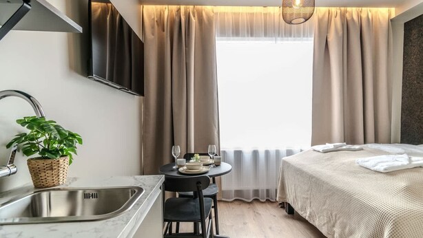 A modern hotel room with a bed, a dining area with a table and chairs, a sink, and a large window with curtains. - Frost Apartments - Standard Studio (Reykjavík)