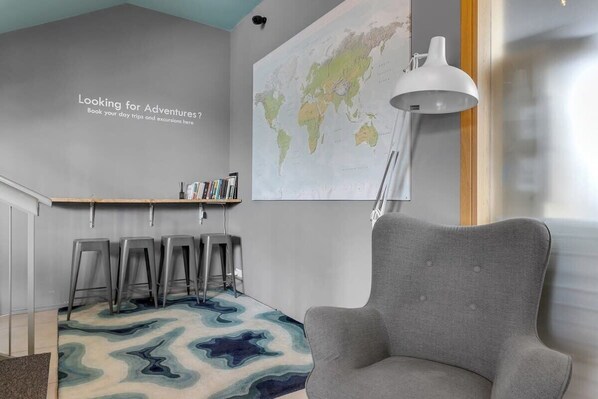 Una habitación moderna con un sillón gris, un mapa del mundo en la pared y una zona de bar con taburetes.