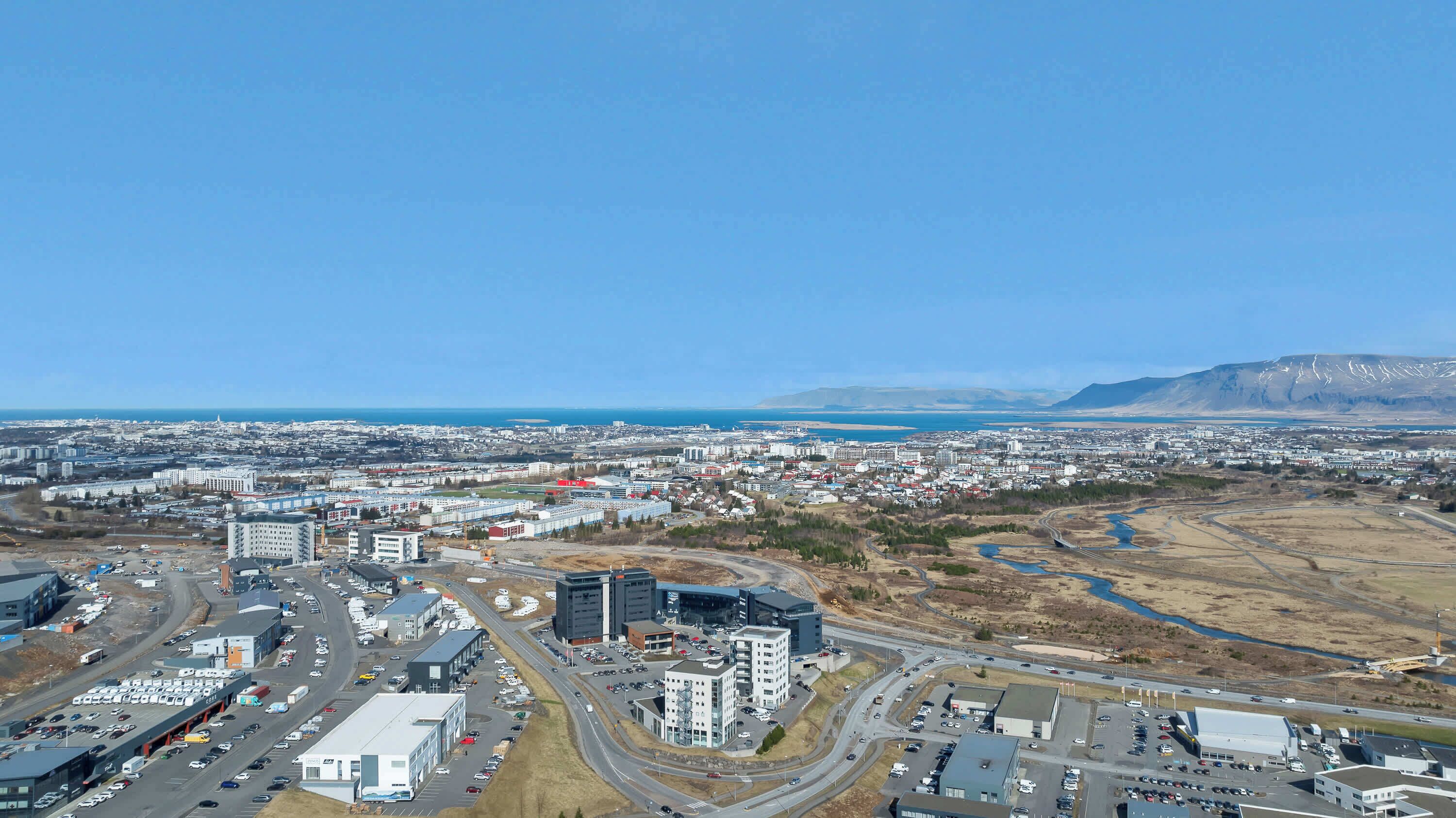 An aerial view of a city with a mix of residential and commercial buildings, a highway, and a body of water in the distance.