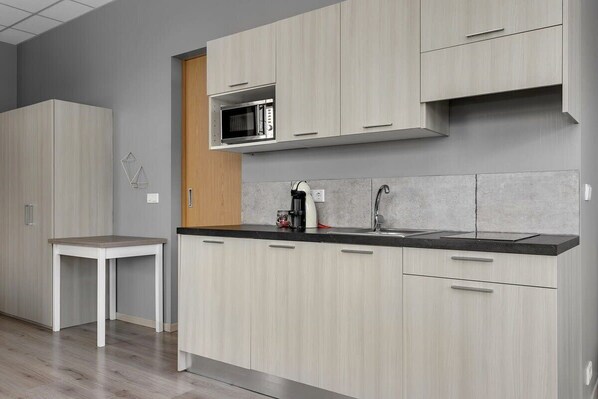 A modern kitchen with light wood cabinets, a black countertop, a microwave, and a coffee machine.