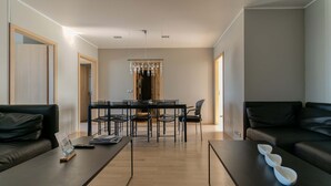 A modern living room with a dining area, featuring a black sofa, a coffee table, and a dining table with chairs.