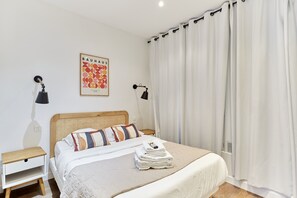 A neatly made bed with a striped pillow, a wall-mounted lamp, and a Bauhaus poster.