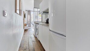A narrow kitchen with white cabinets, a washing machine, and a refrigerator.