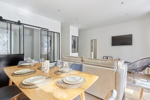 A modern dining area with a wooden table set for four, a sofa, and a TV mounted on the wall.