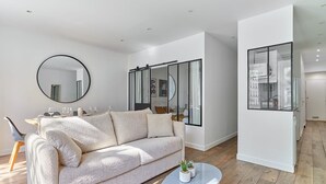 A modern living room with a beige sofa, a round mirror, and a glass partition.