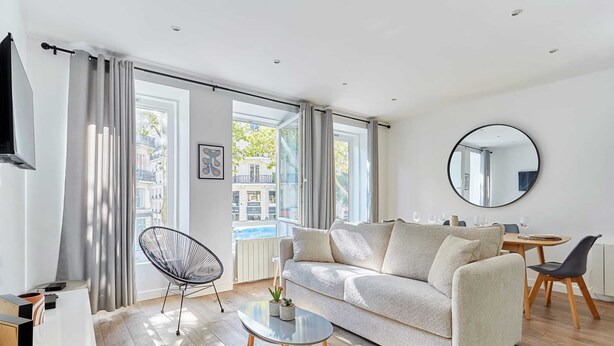 A modern living room with a sofa, a coffee table, and a dining area with chairs and a table.