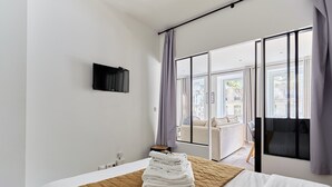A hotel room with a bed, a TV mounted on the wall, and a view of the outside balcony.