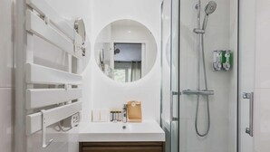 Un bagno moderno con box doccia in vetro, uno specchio rotondo e un lavandino bianco con articoli da toilette.