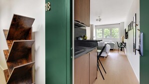 Una cucina moderna con un piano di lavoro nero, mobili in legno e vista su una camera da letto con un letto e una finestra.