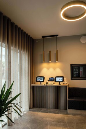 Bancada de recepção com dois monitores, um telefone e uma luminária circular acima.