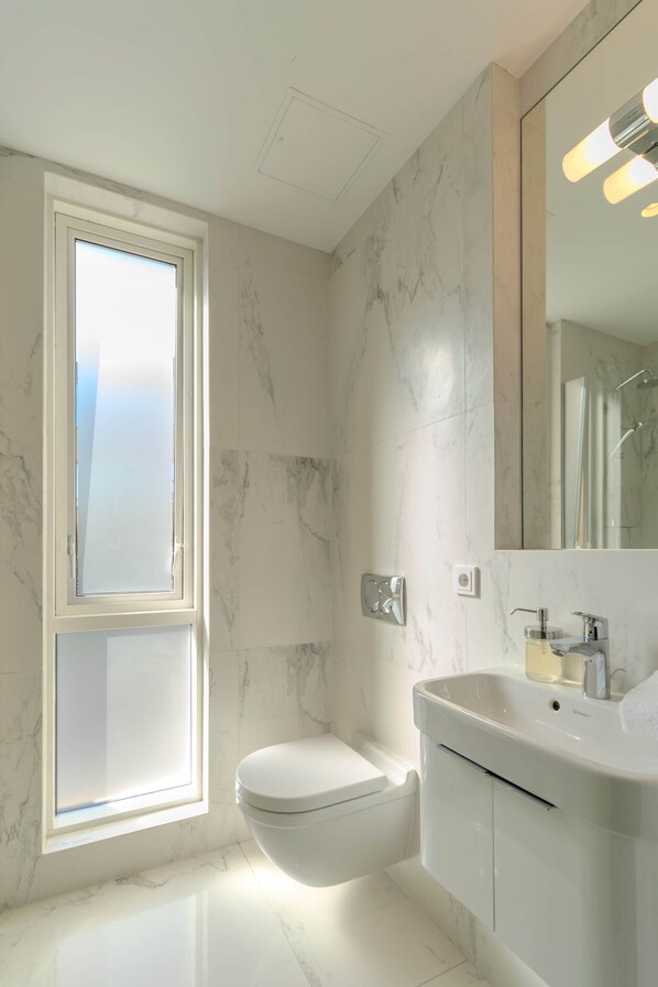 A bathroom with a toilet, a sink, a mirror, and a window.