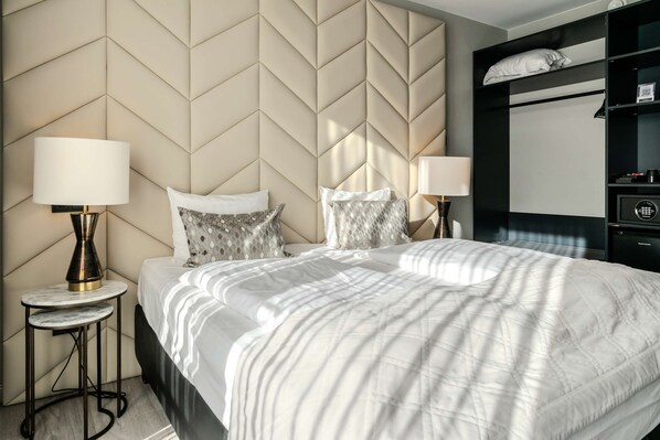 Une chambre d’hôtel comprenant un lit, deux tables de chevet avec des lampes, une tête de lit ornée d’un motif géométrique et une armoire intégrée.
