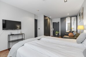 Ein modernes Hotelzimmer mit einem großen Bett, einem Flachbildfernseher an der Wand, einem Nachttisch mit Lampe sowie einer Tür zu einem Badezimmer.
