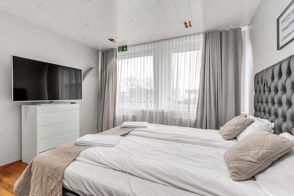 A hotel room with a bed, a television, a white dresser, and a window with curtains.