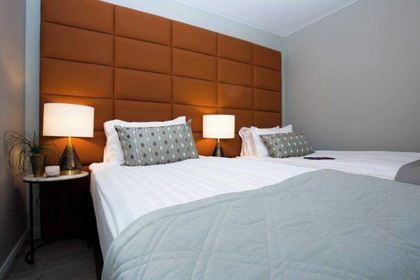 Een hotelkamer met twee bedden, een hoofdbord, bedlampen en een tafeltje met een plant.