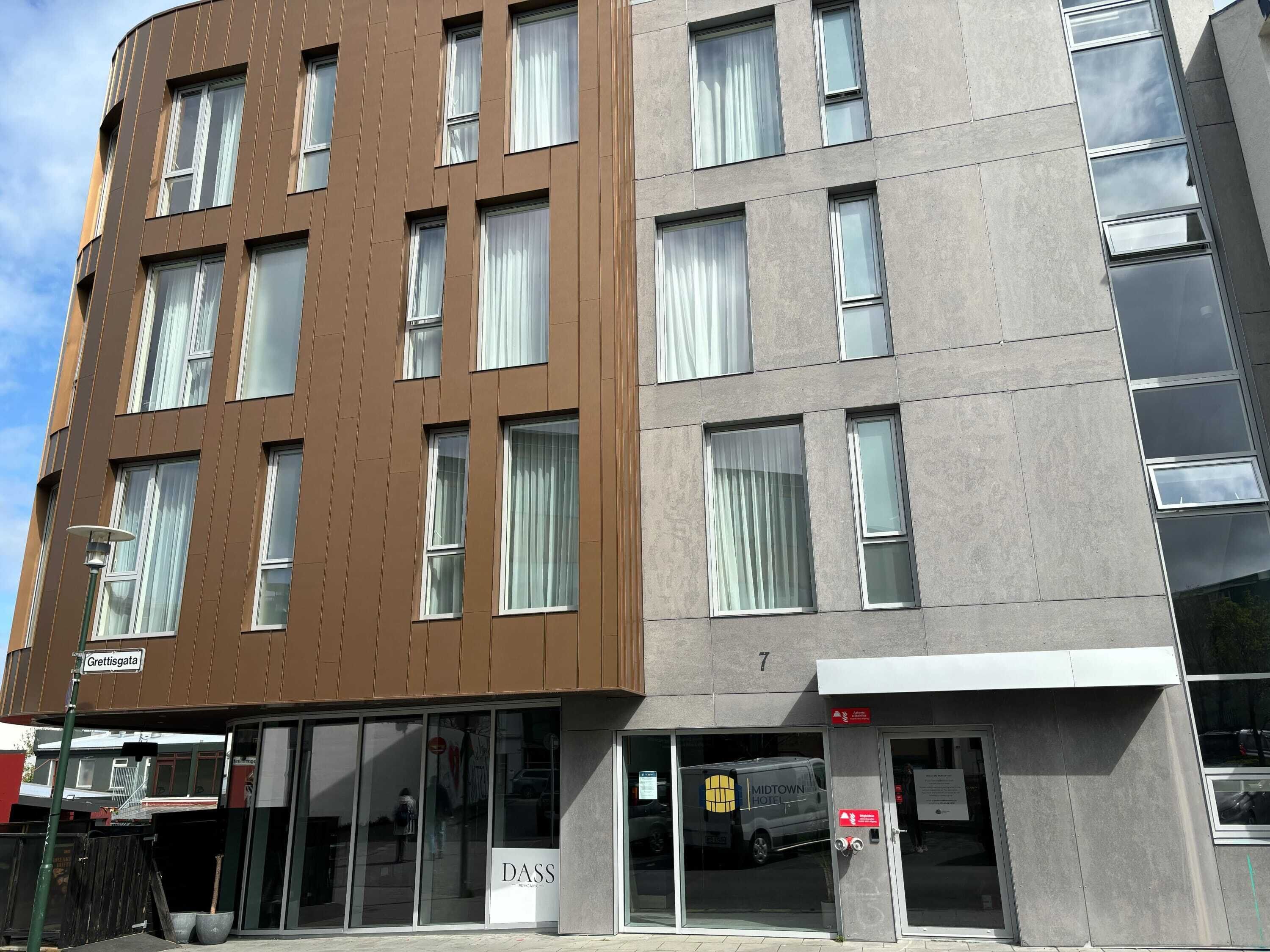 A modern hotel with a brown and gray facade, large windows, and a visible entrance with a sign.