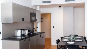 A modern kitchen with grey cabinets, a black countertop, and a dining area with a table set for six. - Sublim Apartment 2 Bedrooms Center of Paris (Paris)