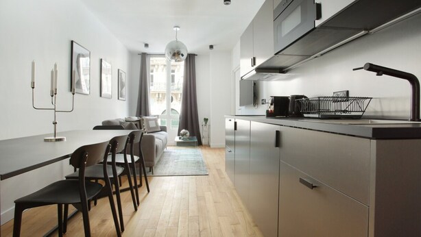 A modern kitchen with stainless steel appliances, a dining area with a long table and chairs, and a view of a balcony through the window. - Sublim Apartment 2 Bedrooms Center of Paris (Paris)