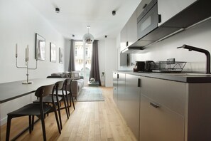 Een moderne keuken met roestvrijstalen apparatuur, een eethoek met een lange tafel en stoelen, en een uitzicht op een balkon door het raam.