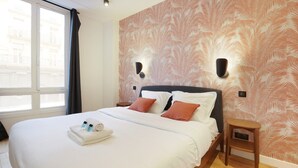 A neatly made bed with white linens and two pillows, a wooden nightstand with a lamp, and a window with curtains. - Sublim Apartment 2 Bedrooms Center of Paris (Paris)