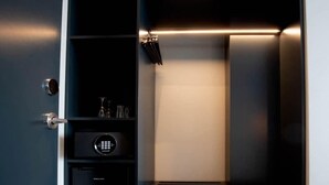 A modern, dimly lit room with a built-in safe, a small seating area, and a door with a handle. - Midtown Reykjavik - Quadruple Room (Reykjavík)