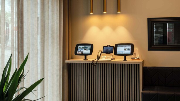 A reception area with a modern design, featuring a reception desk, two monitors, a telephone, and a circular light fixture above.