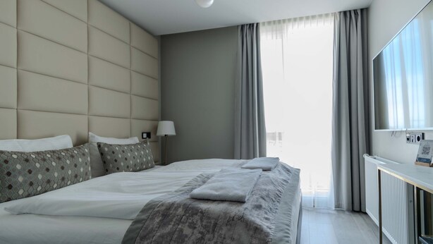 Une chambre d’hôtel moderne avec un grand lit, une table de chevet, une lampe et une vue sur la ville grâce à de grandes fenêtres.