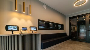 Un espace d’accueil au design moderne, comprenant un comptoir d’accueil doté d’écrans numériques, un téléphone et un coin salon avec un banc.