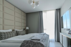 Una habitación de hotel moderna con una cama grande, una mesita de noche, una lámpara y vistas a la ciudad a través de grandes ventanales.