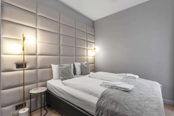 Un dormitorio moderno con cabecera capitonada, mesita de noche redonda y una cama impecable con manta acolchada.