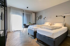 Hotellihuone, jossa on kaksi sänkyä, työpöytä, tuoli ja suuri ikkuna, jossa on verhot.