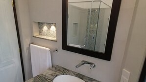 Een moderne badkamer met een marmeren wastafel, een grote spiegel en een douchecabine van glas.