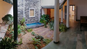 Een binnentuin met een stenen muur, een klein waterpartij en verschillende planten.