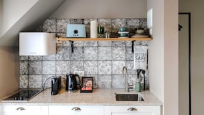 A modern kitchen with a built-in stove, a coffee machine, and a kettle on the countertop. There is a shelf above the sink with decorative items and a sign that reads "Better Safe Than Sorry." - Saga Studio with Balcony for 2 guests in Downtown (Reykjavík)