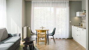 A modern living room with a sofa, a dining table with chairs, and a kitchen area with cabinets and a countertop.