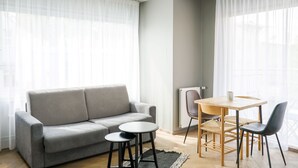 A modern living room with a grey sofa, a small round table, two chairs, and a radiator.