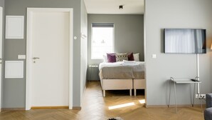 A bedroom with a bed, a TV, a desk, and a window.