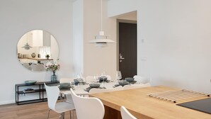 A modern dining area with a round mirror, white chairs, a wooden table, and a hanging light fixture.