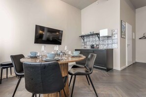 A modern dining area with a round wooden table, black chairs, and a kitchen with patterned tiles in the background.