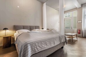 A modern bedroom with a large bed, a bedside table, a lamp, and a view of the outside.
