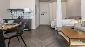 Un espacio habitable compacto con kitchenette, una zona de comedor con mesa y sillas, una cama con dosel y un sofá.