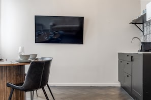 A modern kitchen with a flat-screen TV mounted on the wall, a dining table with chairs, and a built-in sink.