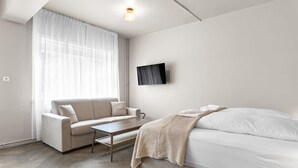 Ein modernes, minimalistisches Schlafzimmer mit Sofa, Bett und einem an der Wand montierten Fernseher.