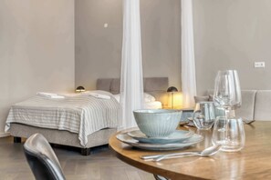 Een hotelkamer met een bed, nachtkastje met een lamp, een eettafel met borden, glazen en bestek.