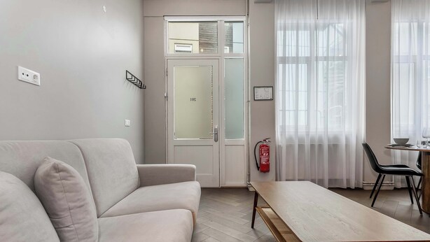 A modern living room with a sofa, a wooden table, and a dining area with a chair and a small table. - Swan Deluxe Studio for 4 guests (Reykjavík)