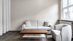 A minimalist living room with a light grey sofa, a wooden coffee table, and a grey armchair. - Swan Deluxe Studio for 4 guests (Reykjavík)