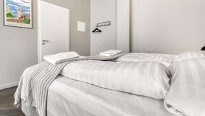 Quarto de hotel com cama, porta, cabideiro e um quadro na parede.