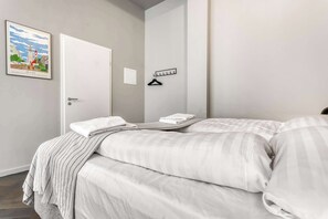 A hotel room with a bed, a door, a coat rack, and a framed picture on the wall.