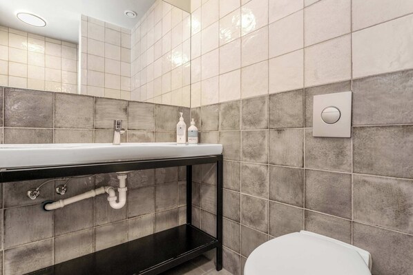 A modern bathroom with a white sink, black countertop, and grey tiled walls.